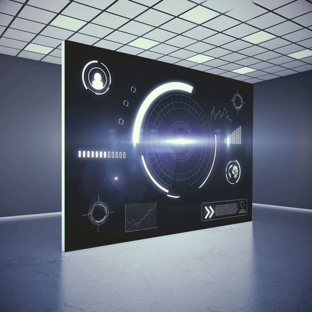 A futuristic, dimly-lit room with a large digital screen displaying various holographic graphs, charts, and circular interface elements. The design is high-tech, with a glowing central circle and light-blue accents.